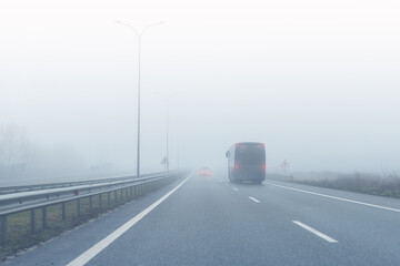 Coach bus on almost empty blue foggy misty rainy highway intercity road with low poor visibility on cold spring autumn morning. Seasonal bad rainy weather accident danger warning. car fog light