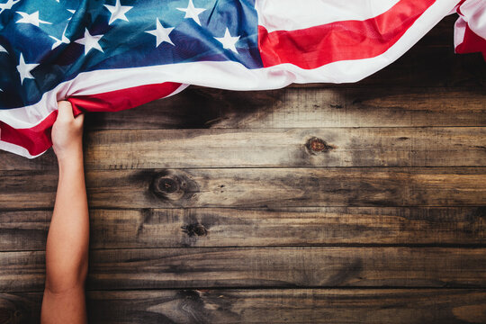 A child's hand holds the flag of the United States of America. Wooden background. Patriotism, Independence Day, July 4th, holiday. Close-up