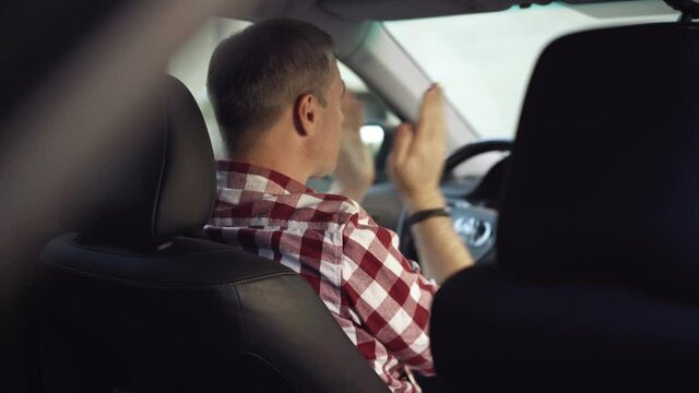 Shooting from back seat of exhausted Caucasian driver slapping cheeks sitting on driver's seat. Tired overworked man waiting for client in taxi. Exhaustion and overworking.