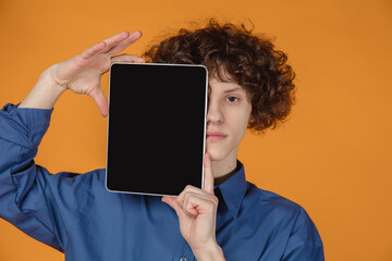 Blank screen. Caucasian handsome young man's portrait isolated on yellow studio background with copyspace. Male model with curly hair. Concept of human emotions, facial expression, sales, ad, fashion.