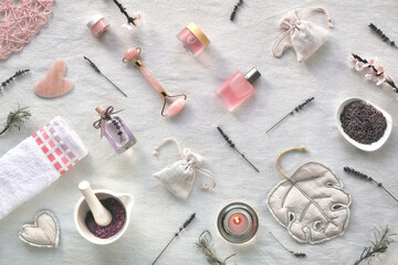 Fototapeta na wymiar Crystal rose quartz roller and Gua sha stone for massage therapy. Pink skincare products, essential oil. Off white textile background, top view. Cherry blossoms on twigs. Geometric arrangement.