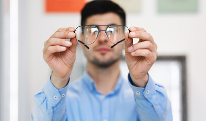 Closeup portrait of young man showing spectacles to camera