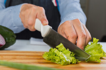 Closeup of hands cutting lettuce on wooden Board.