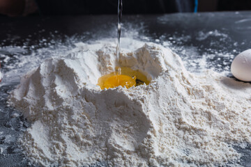 Hands putting an egg in flour preparing to make a dough.
