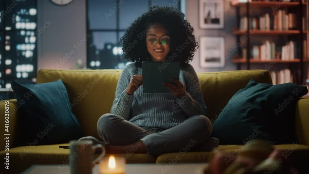 Poster beautiful authentic latina female sitting on couch sofa in a cozy dark living room in the evening an