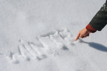 A man in a coat writes with his hand, draws letters and the word winter on the white fresh snow. Photography, concept, top view.