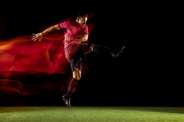 Powerful, flying above the field. Young football, soccer player in action, motion on black...
