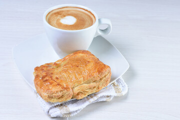 Cup of Colombian coffee, accompanied by baked bakery on white wooden background