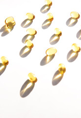 Shiny yellow fish oil capsules isolated on a white background with shadows of focus on the table. Vitamin E. Copy space for your text