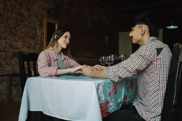 Beautiful young couple holding hands, looking at each other and smiling during their date in a restaurant.