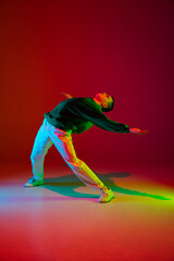 Freedom. Stylish sportive boy dancing hip-hop in stylish clothes on colorful background at dance hall in neon light. Youth culture, movement, style and fashion, action. Fashionable bright portrait.