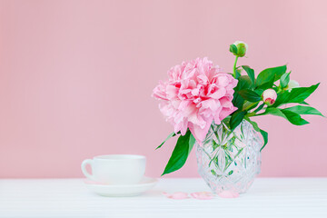 Pink peonies in a crystal vase on a pink wood background.