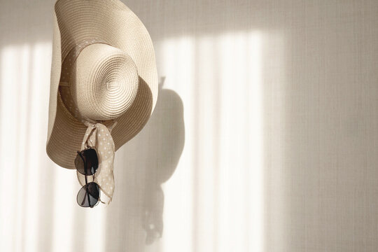 Women straw hat and sunglasses hang on background white wall with shadow. Summer beach fashion concept. Copy space