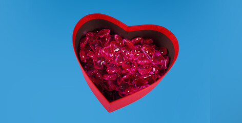 Close up of lots of hearts in red gift box in form of heart. Small red hearts in box for present on blue background. Concept of goodness, love and charity.