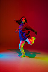 Fototapeta na wymiar Freedom. Stylish sportive girl dancing hip-hop in stylish clothes on colorful background at dance hall in neon light. Youth culture, movement, style and fashion, action. Fashionable bright portrait.