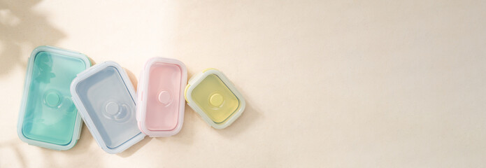 Banner of pastel reusable and foldable silicone lunch box and food container on the table with sunlight shine on. Reduce waste, Better world, Zero waste campaign. Top view close up with copy space.