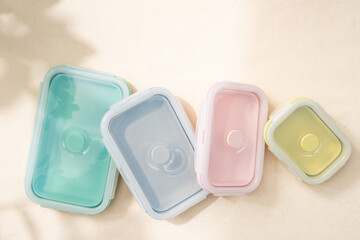 A set of pastel reusable and foldable silicone lunch box and food container on the table with sunlight shine on. Reduce waste, Better world, Zero waste campaign. Top view close up with copy space.
