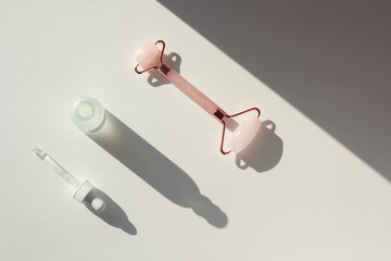 Concept of minimalistic skincare routine (skinimalism). Flat lay with serum and rose quartz roller with contrasting shadows.