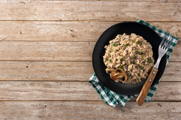 Risotto with mushroom on black plate on wooden table. Top view. Copy space