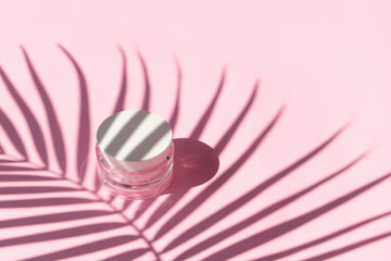 Jar of cream with palm leaf shadow on pink background