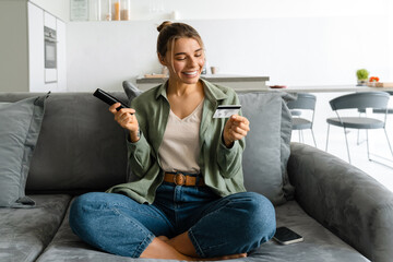 Happy woman holding credit card while watching TV with remote control