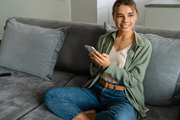 Happy nice woman using mobile phone while sitting on sofa