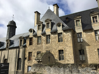 Fototapeta premium Bayeux, France. September, 11, 2017. The gray-yellow facade of a part of the Cathedral Norte-Dame de Bayeux, with small windows and a dark roof with decorated windows on it.