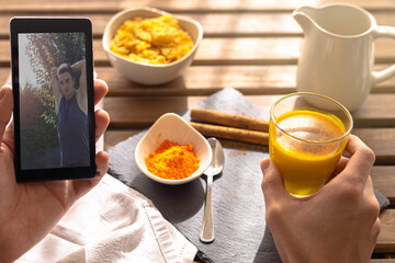 Selective focus on a person having an energetic breakfast of cereal with golden milk, turmeric cereal and Indian cinnamon while looking at a cell phone, a guy stretching and exercising on a wooden tab