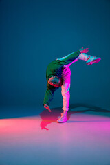 Flexible. Stylish sportive boy dancing hip-hop in stylish clothes on colorful background at dance...