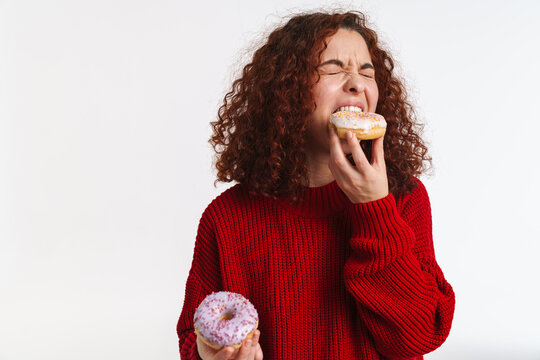 Excited Ginger Young Woman Grimacing While Eating Doughnuts