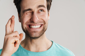 Joyful guy winking while holding fingers crossed for good luck