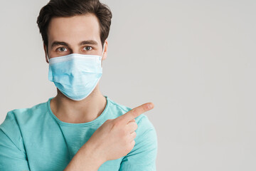 Caucasian handsome guy in protective mask pointing finger aside