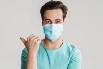 Caucasian handsome guy in protective mask pointing finger aside