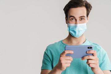 Pleased handsome guy in protective mask using mobile phone