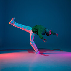 Inspired. Stylish sportive boy dancing hip-hop in stylish clothes on colorful background at dance hall in neon light. Youth culture, movement, style and fashion, action. Fashionable bright portrait.