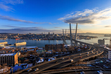 Vladivostok, Russia, 2017 - Golden Bridge during sunset against the background of the central part of the city. Bright beautiful sunset over the sea city in winter.