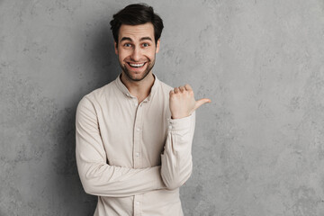 Joyful handsome guy smiling and pointing finger aside