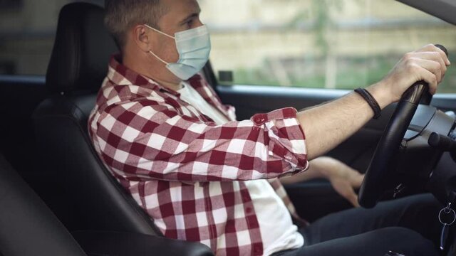 Adult man sitting on driver's seat in car, taking off Covid face mask, and sighing. Portrait of tired Caucasian guy in vehicle on coronavirus pandemic. Health protection and new normal lifestyle.