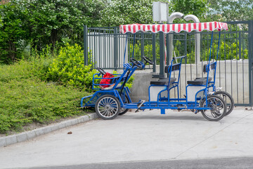 A multi-seat tandem bike with a red and white striped canopy is rented in the parking lot. Budapest, Hungary.