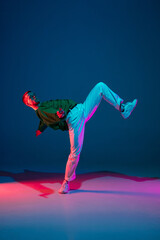 Modern. Stylish sportive boy dancing hip-hop in stylish clothes on colorful background at dance hall in neon light. Youth culture, movement, style and fashion, action. Fashionable bright portrait.