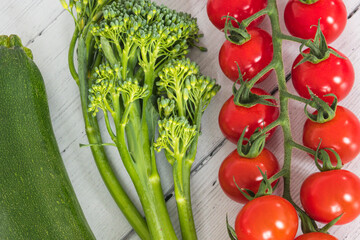 Tender stem Broccoli a small string of tomatoes and a Single Courgette lying on a white board