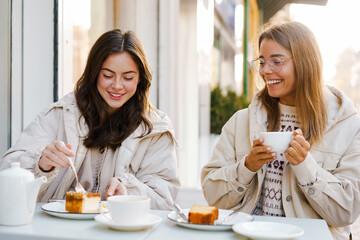 Two cheerful attractive women friends having tea and cakes