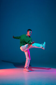 Modern. Stylish sportive boy dancing hip-hop in stylish clothes on colorful background at dance hall in neon light. Youth culture, movement, style and fashion, action. Fashionable bright portrait.