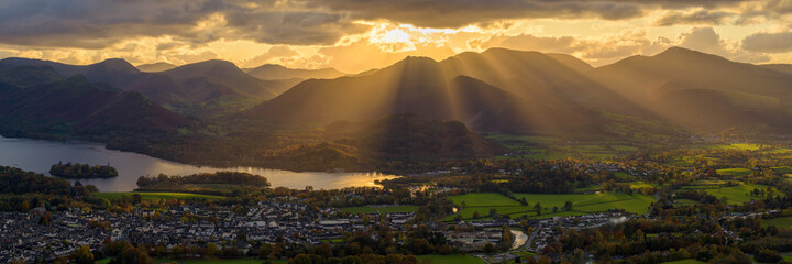 Golden rays of light breaking through clouds over Derwentwater and Keswick in the Lake District.