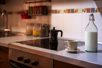 Cup of coffee next to a glass bottle with milk on the kitchen countertop.