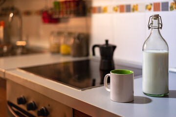 Cup of coffee next to a glass bottle with milk on the kitchen countertop.