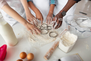 Cutting out round shapes from rolled out dough to prepare home made cookies. Hands of multiethnic family cutting raw dough with metal cutters