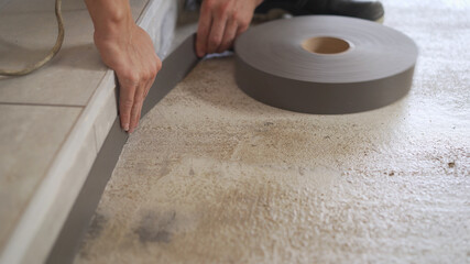 The worker glues the tape to the floor around the room. Construction concept. Installing plinth on...