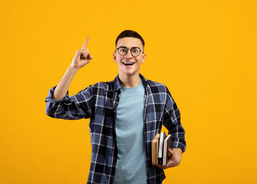 Millennial student with books having creative idea, showing eureka gesture, experiencing AHA moment on orange background