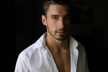 Portrait of handsome man with beard standing next to window with open shirt